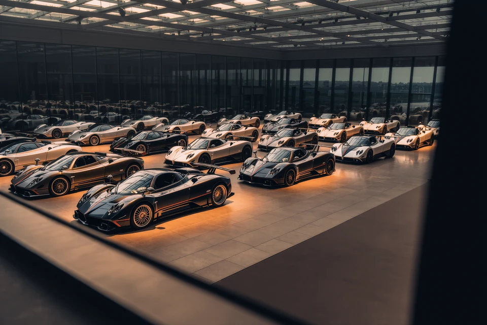 Indoor car exhibition at Motorworld Mallorca featuring vintage and modern vehicles on display, surrounded by visitors walking and observing under stylish artificial palm trees.