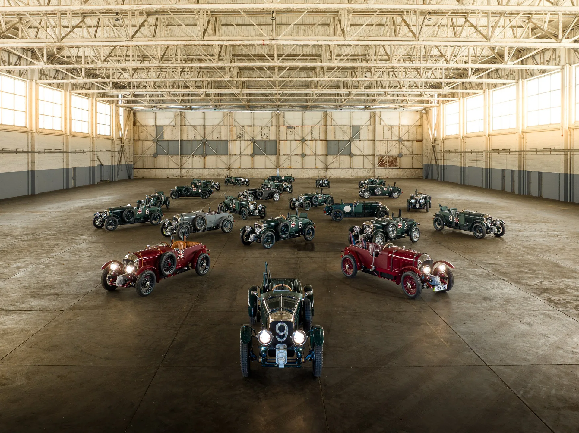 Several green and red Bentley Blower Jnr cars lined up in a large hall