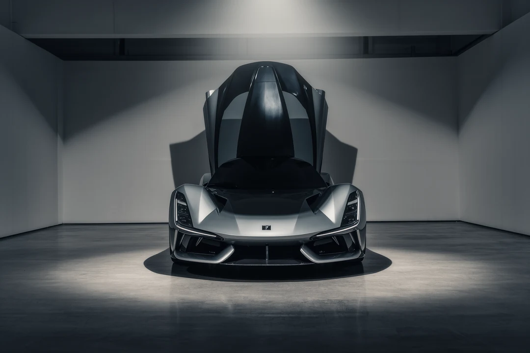 A sleek supercar parked outside a modern glass building on a racetrack, with sunlight reflecting off the windows and a clear sky in the background.